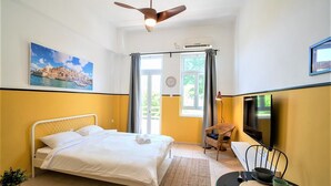 Hotellihuone, jossa on sänky, tuoli, pöytä, jossa on kulho ja muki, televisio ja taulu seinällä.