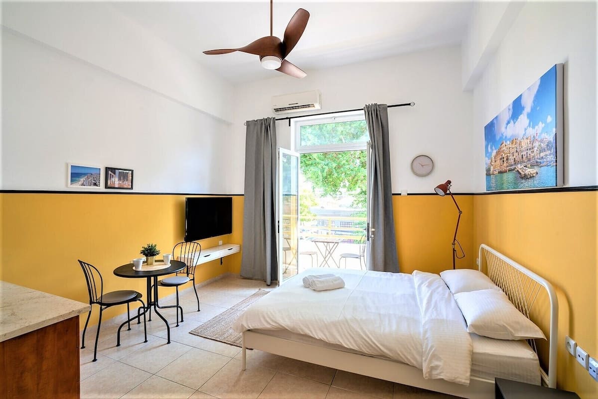 A hotel room with a bed, a desk with a chair, a TV, and a painting on the wall.
