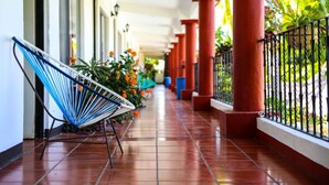 A covered corridor with red pillars, a hammock chair, and potted plants. - Hotel Albatros (Puerto Escondido)