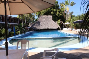 A swimming pool with a thatched roof, surrounded by palm trees and a building with balconies. - Hotel Albatros (Puerto Escondido)