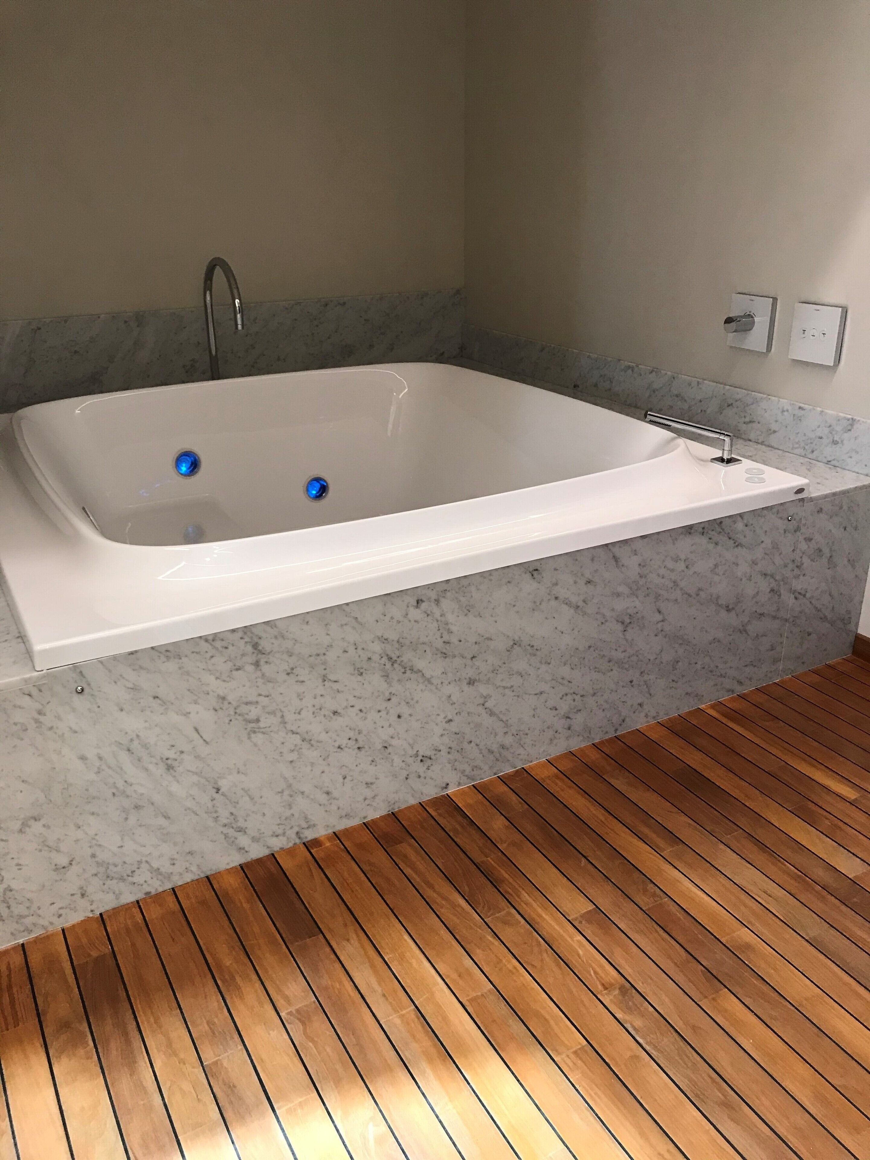 Un baño moderno con una bañera independiente, encimera de mármol y suelo de madera.