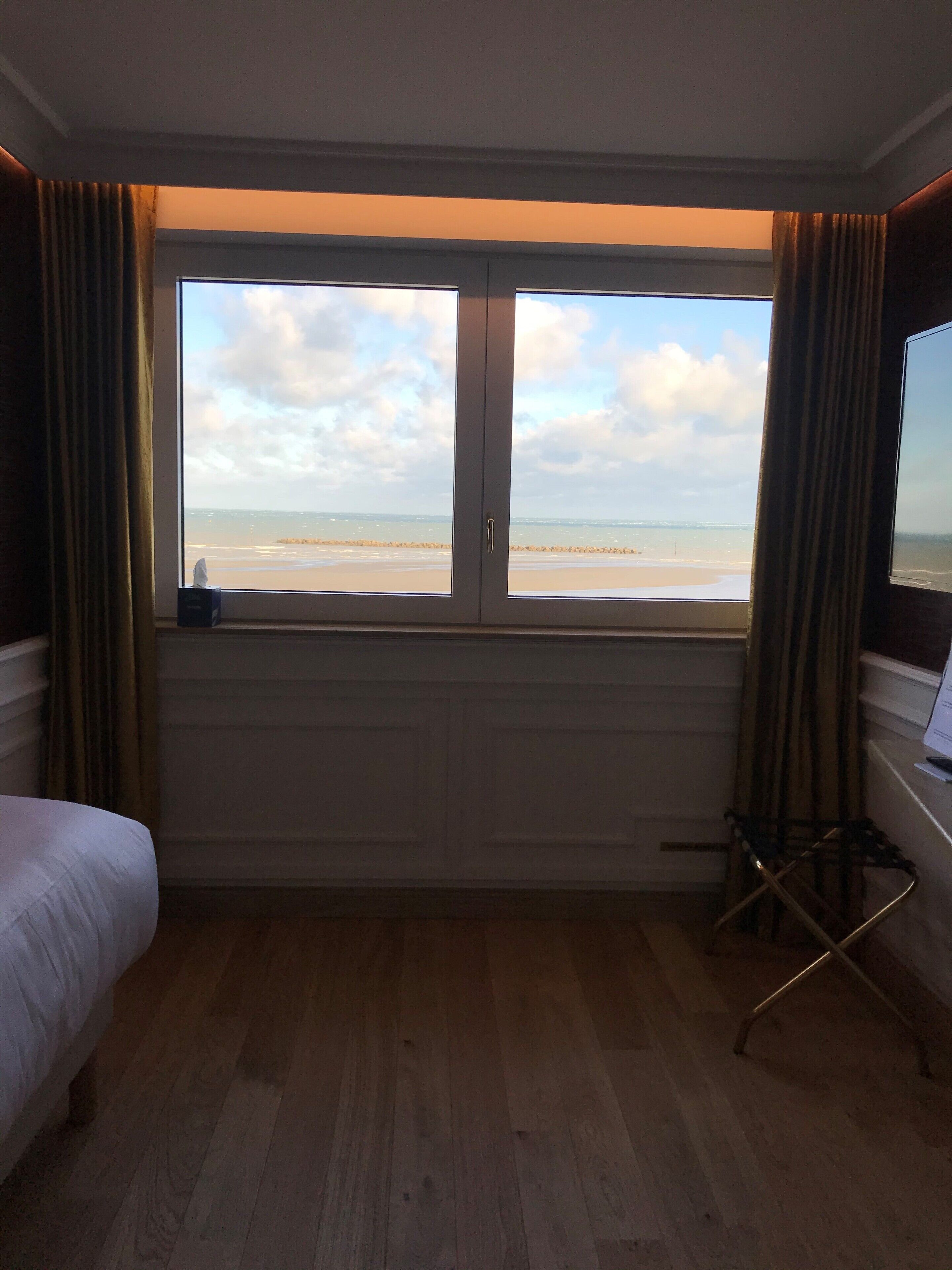 Hotelkamer met een groot raam dat uitzicht biedt op het strand, een bed, een stoel en een bureau.