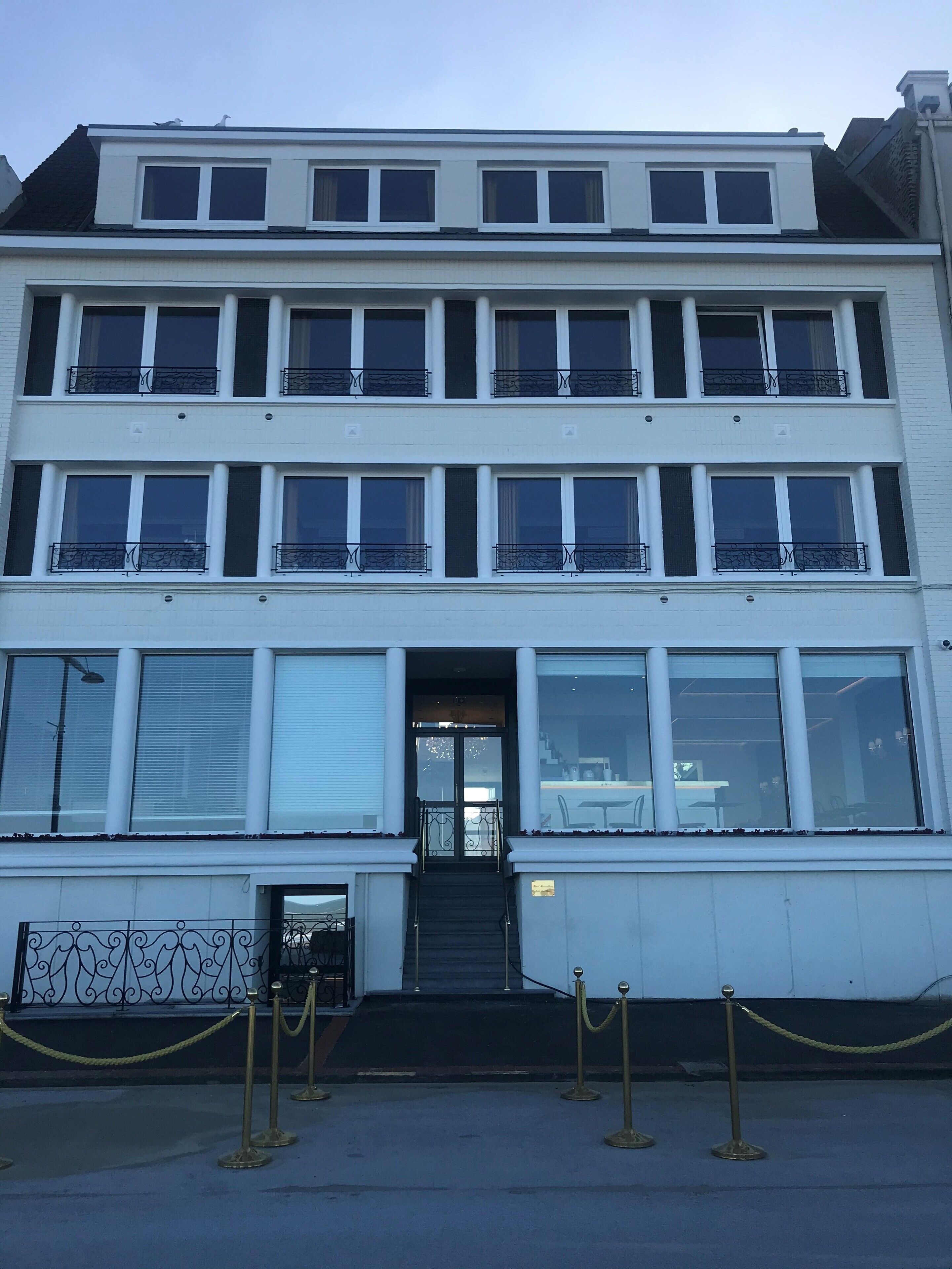 Un edificio de varios pisos con fachada simétrica, ventanas amplias y una entrada central con escalones.