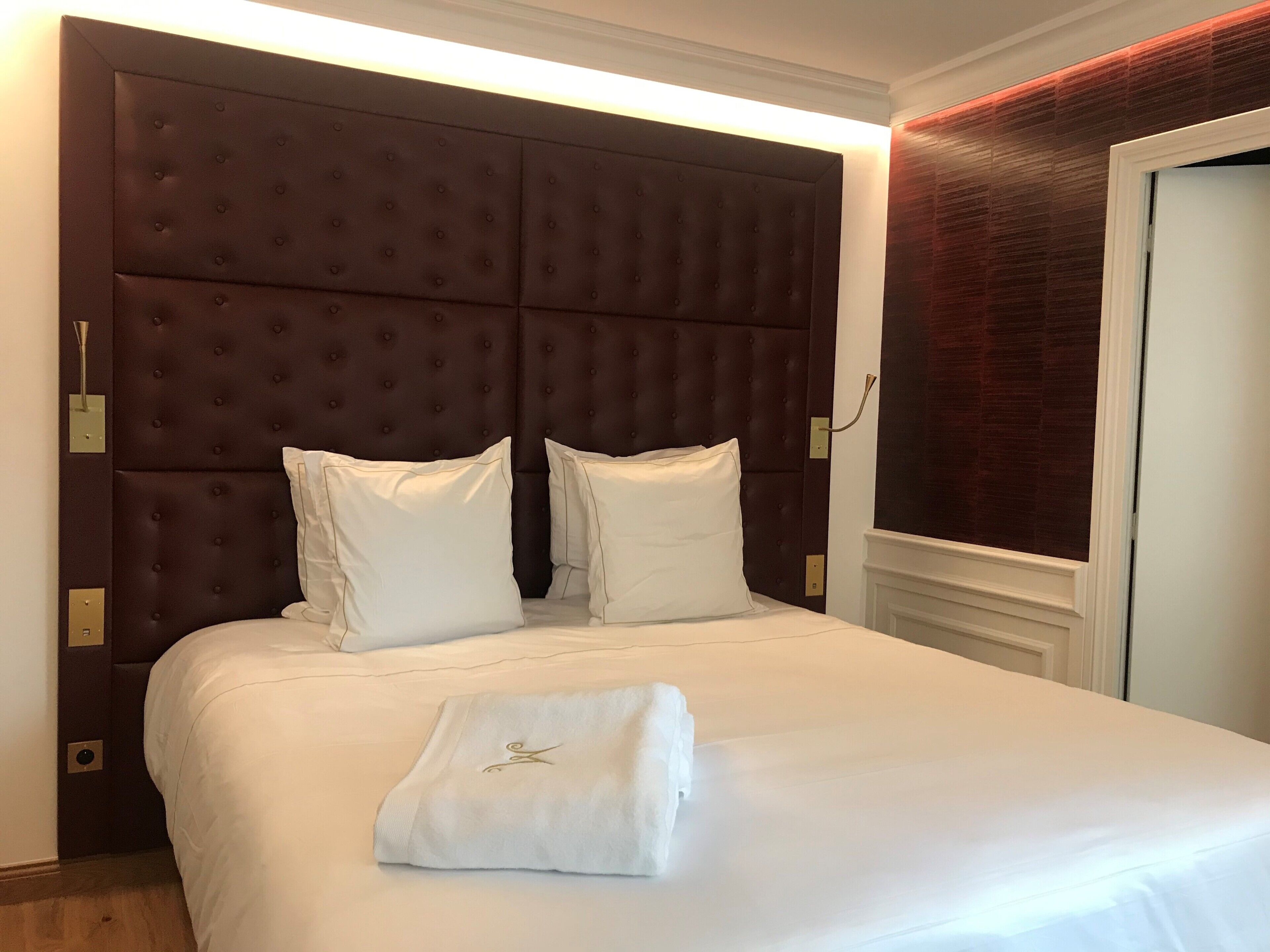 Una cama bien hecha con un gran cabecero capitonado, dos almohadas y una toalla doblada sobre la cama.