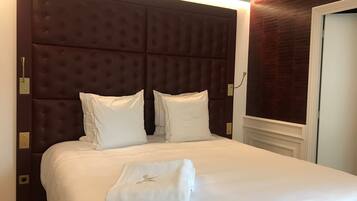 A neatly made bed with a large, tufted headboard, two pillows, and a folded towel on the bed.