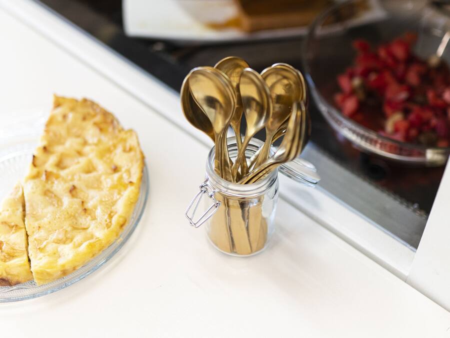 Un plat en verre contenant une part de tarte, un porte-cuillère en métal, un panier de fruits et un bol de fraises, le tout posé sur un comptoir blanc.