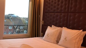A neatly made bed with white linens and pillows, a large window with a view of buildings, and a dark brown headboard. - Hotel Merveilleux Côté Mer (Dunkirk)