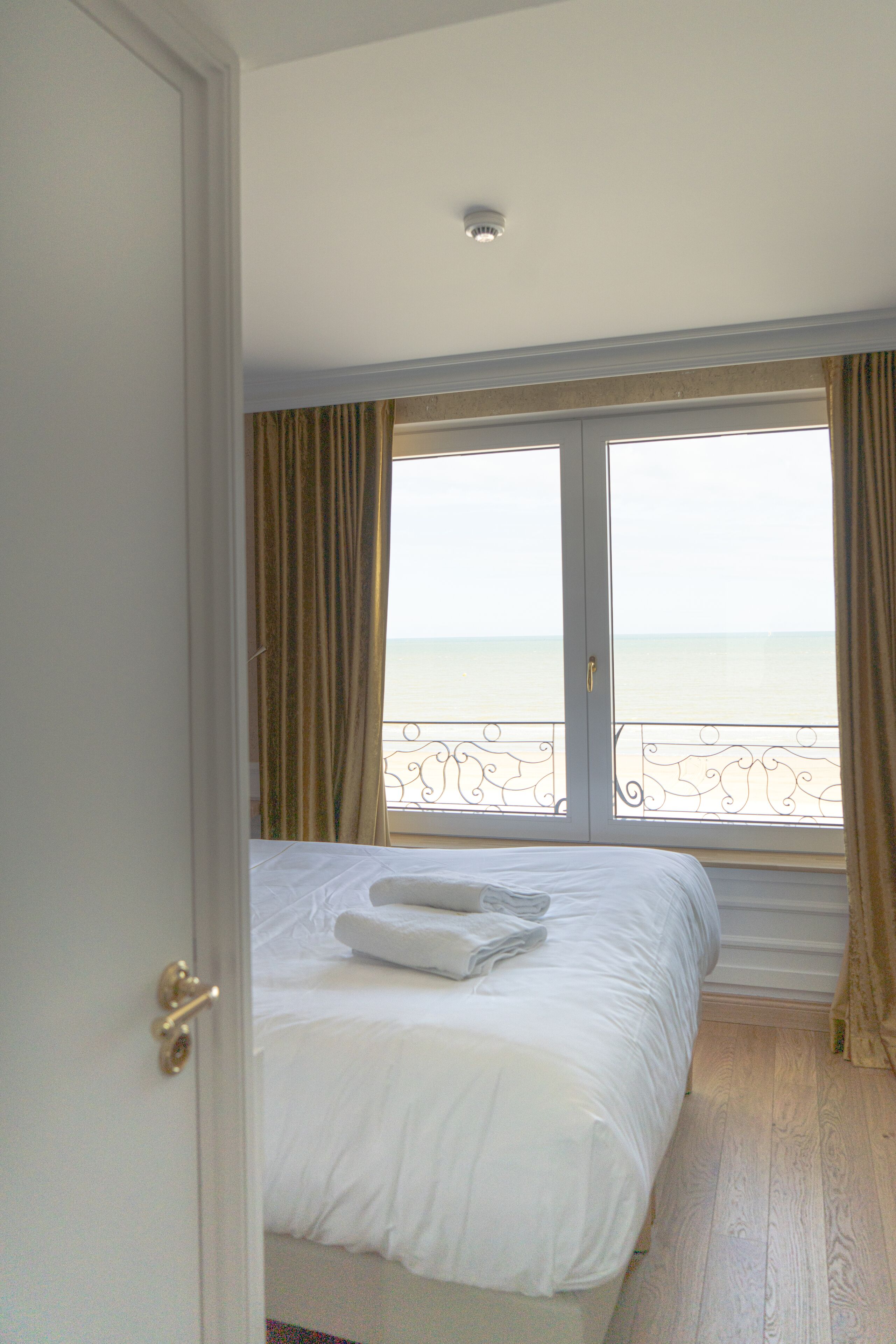 Ein Hotelzimmer mit einem großen Bett, Meerblick von einem Balkon und einer Tür zum Zimmer.