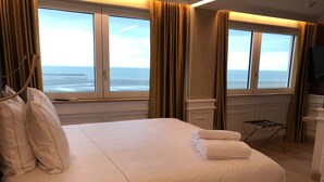 A hotel room with a large bed, a view of the sea, and a small desk with a chair. - Hotel Merveilleux Côté Mer (Dunkirk)