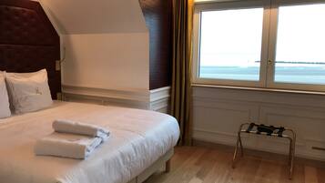 Una habitación de hotel con una cama grande, un ventanal con vista al mar y un taburete cerca de la ventana.