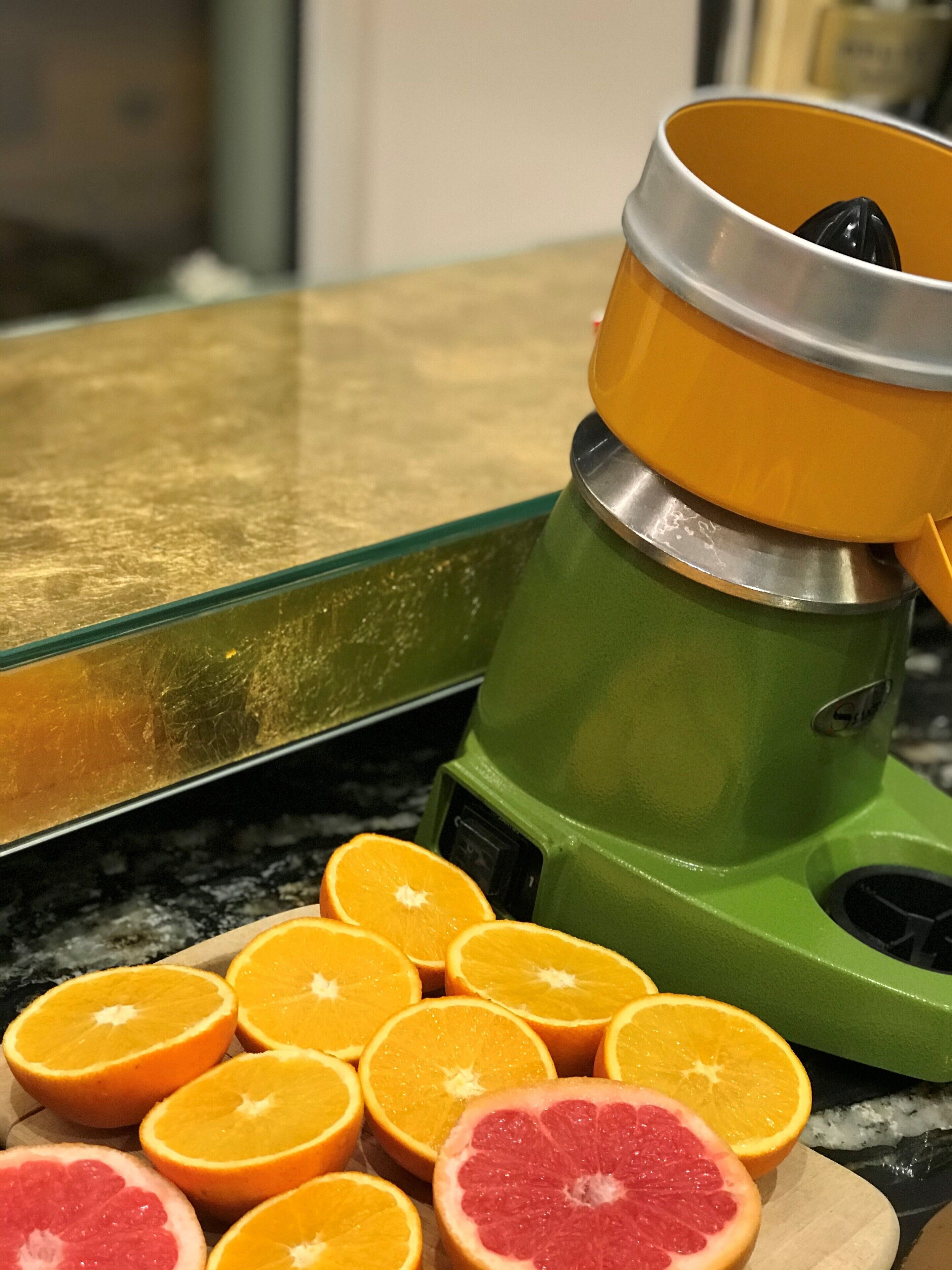 A kitchen counter with a juicer and sliced oranges and grapefruit.