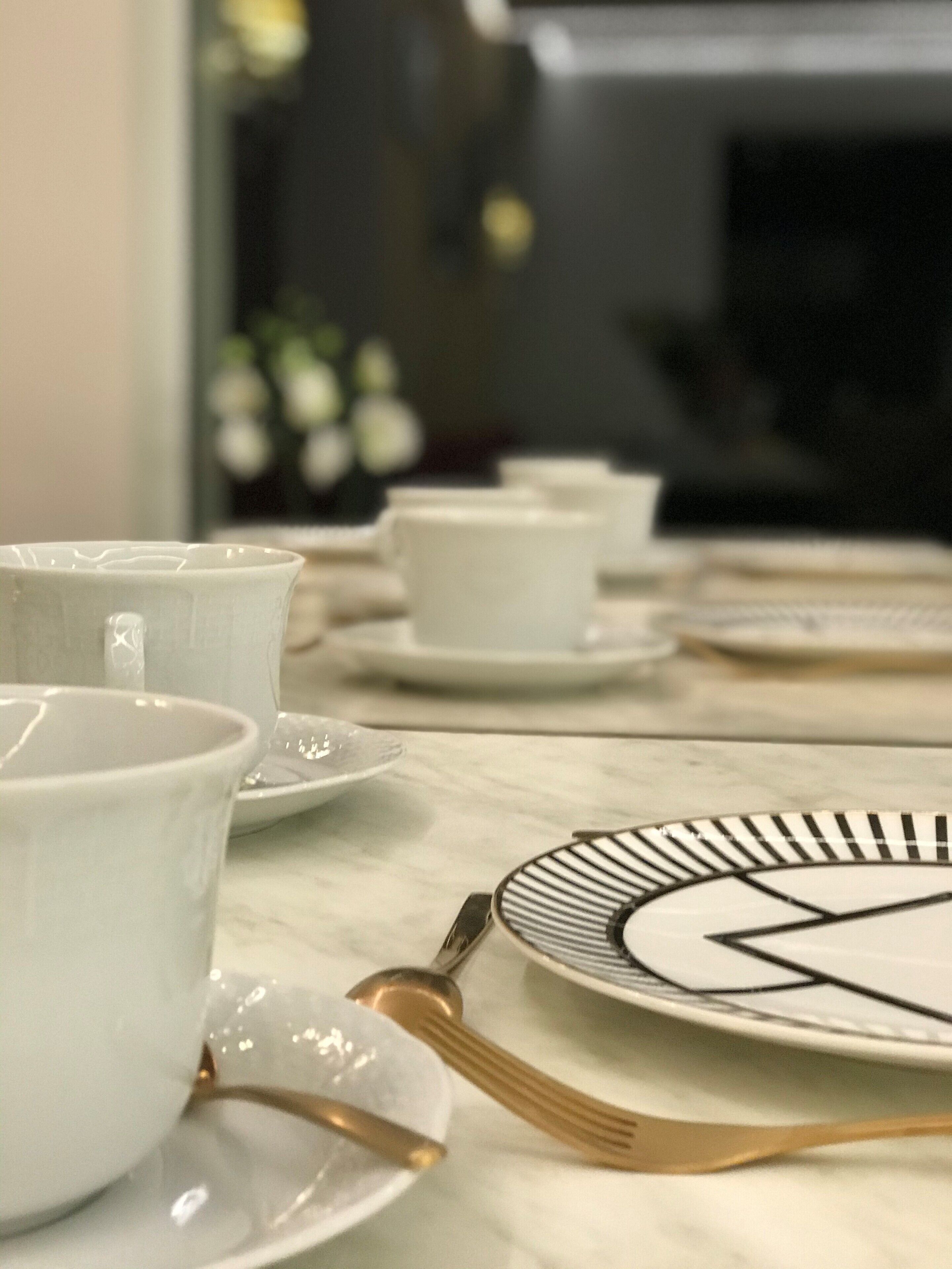 Una mesa dispuesta con tazas y platillos de cerámica blanca, y un tenedor de mango dorado sobre una mesa de mármol.