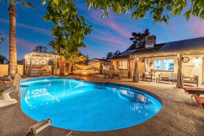 Ein Swimmingpool mit einer Liegeinsel, Gartenmöbeln und einer überdachten Terrasse.