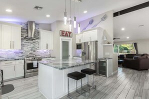 A modern kitchen with white cabinets, a central island with bar stools, stainless steel appliances, and a backsplash with a mosaic pattern.