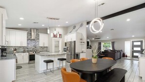 Une cuisine moderne avec des meubles blancs, un îlot central et un coin repas agrémenté de chaises orange.