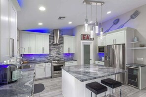 A modern kitchen with white cabinets, a marble island, stainless steel appliances, and blue under-cabinet lighting.