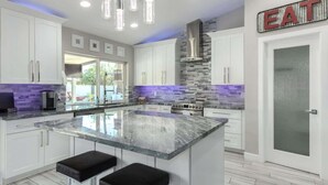 Une cuisine moderne avec des meubles blancs, un grand îlot central doté de tabourets, un pare-feu en pierre et des luminaires suspendus.