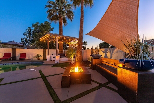 Relax by the fire pit in a tranquil outdoor space surrounded by seating and a pool.