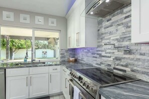 A modern kitchen with white cabinets, a black stove, and a stone backsplash.
