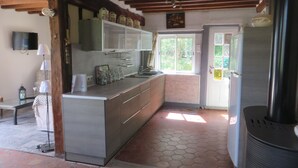 Una cocina con piso de baldosas, vigas de madera, estufa integrada y una ventana con vista a follaje.
