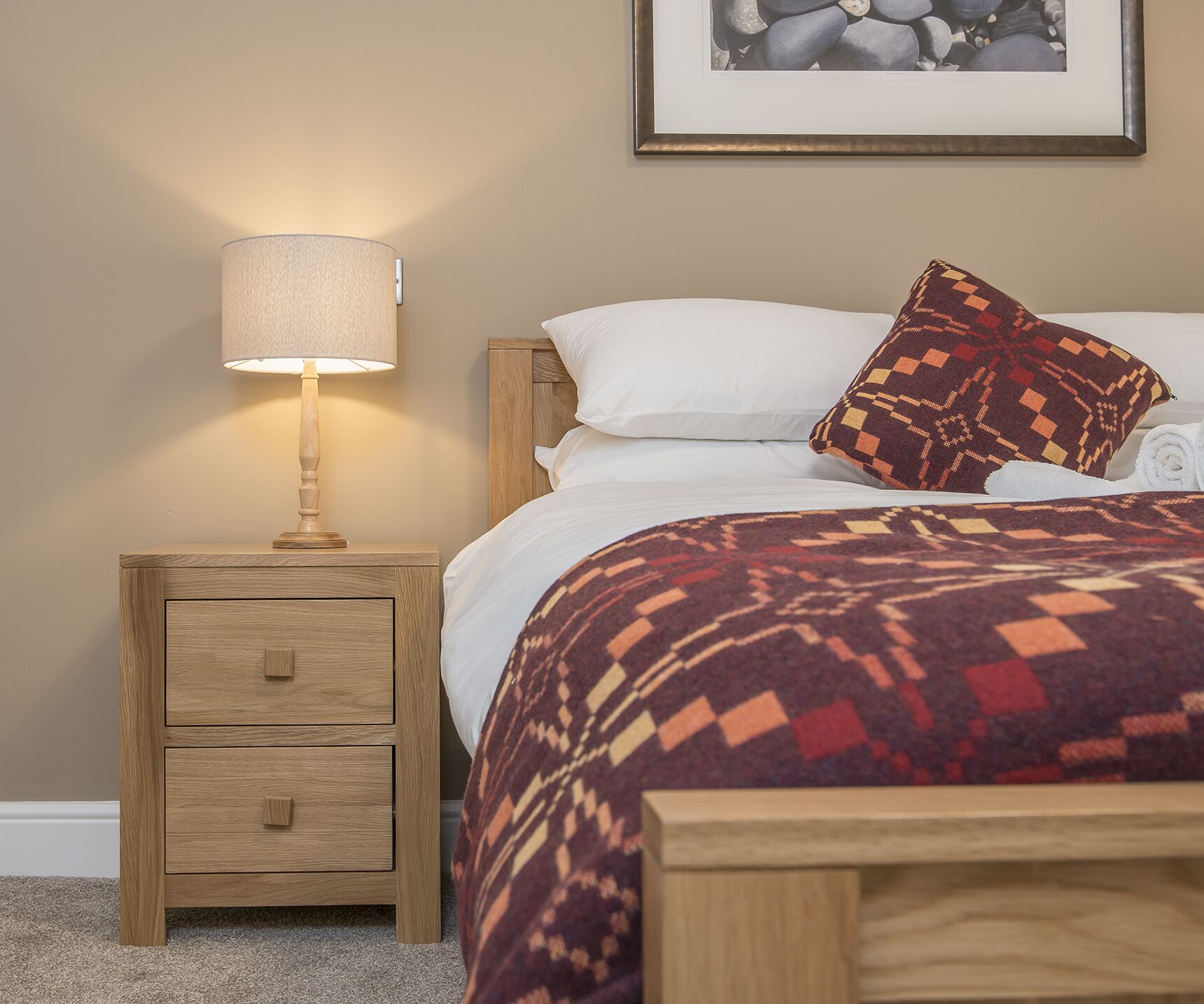 A neatly made bed with a patterned blanket, a bedside lamp, and a small wooden nightstand with drawers.