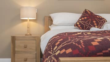 A neatly made bed with a patterned blanket, a bedside lamp, and a small wooden nightstand with drawers.