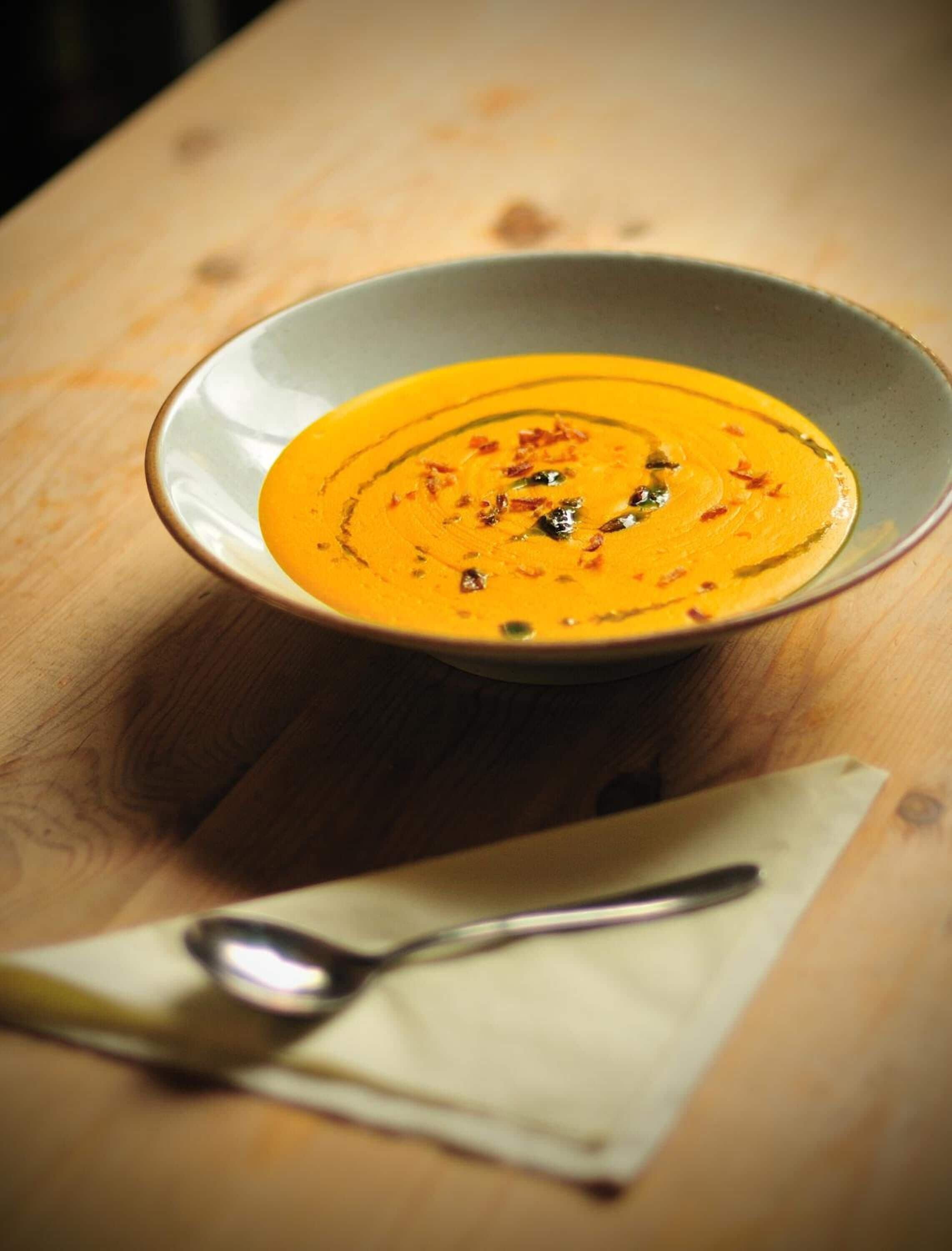 A bowl of soup on a wooden table with a spoon and napkin beside it.