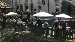 A courtyard with a wooden fence, outdoor seating under umbrellas, and a building with multiple windows and a sign. - The Nag's Head Inn (Boncath)