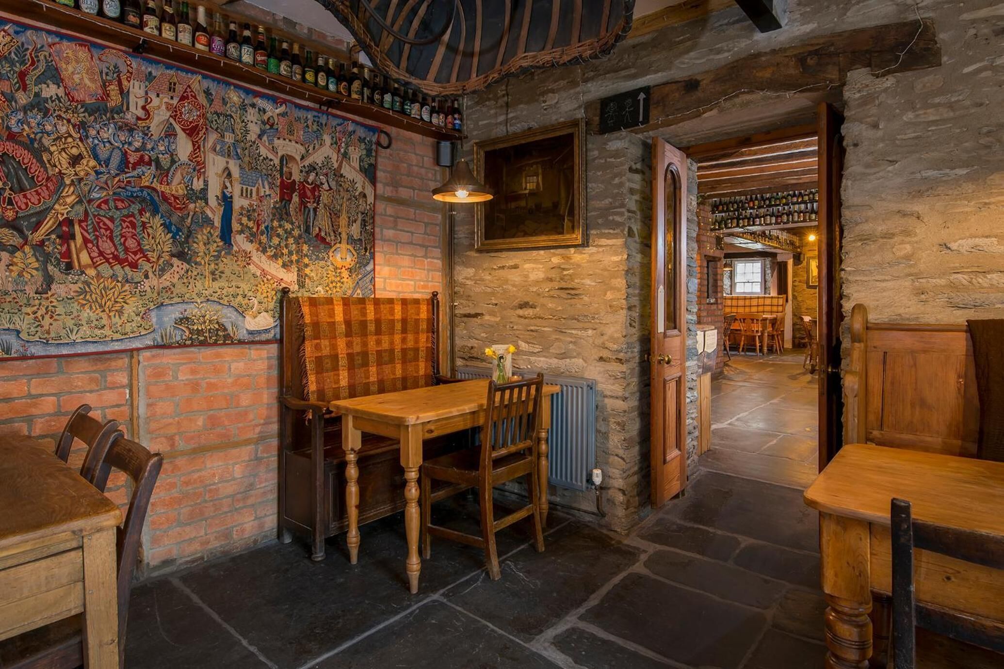 A rustic interior with a stone wall, a large tapestry, and wooden furniture.