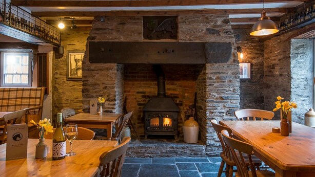 A rustic interior with a stone fireplace, wooden furniture, and a balcony with a railing. - The Nag's Head Inn (Boncath)