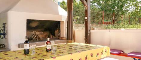An outdoor patio with a barbecue grill, a table with a fruit-patterned tablecloth, and purple cushioned benches.