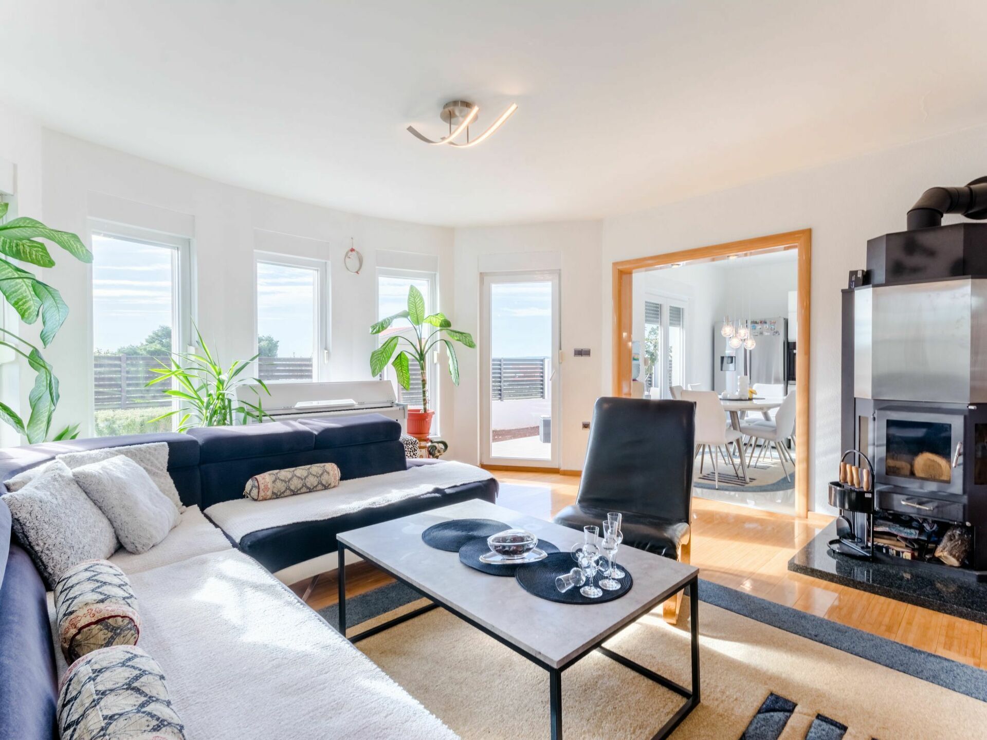 Una sala de estar moderna con sofá, mesa de centro y chimenea. Amplias ventanas ofrecen vistas al exterior.