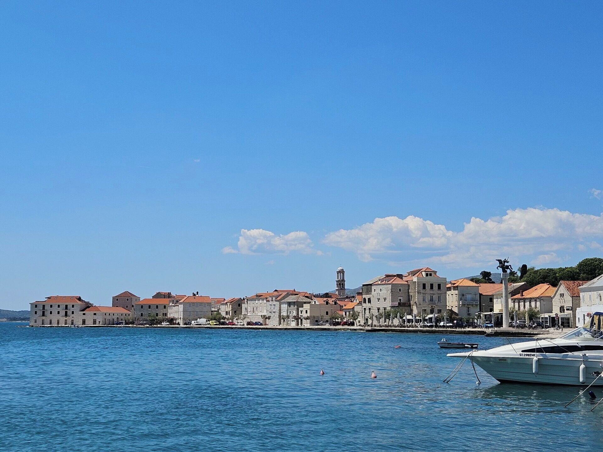 Uma cidade costeira com edifícios ao longo da orla, céu claro e mar calmo.