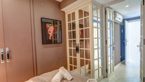 Een hotelkamer met een bed, een schilderij, een kledingkast en een glazen deur die uitkomt op een gang.