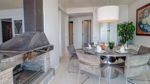 Een moderne eetruimte met een ronde tafel, grijs gestoffeerde stoelen en een grote hanglamp.