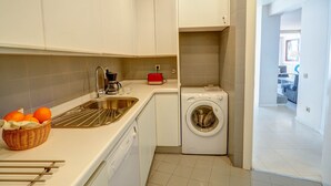 Een moderne keuken met witte kastjes, een roestvrijstalen spoelbak, een wasmachine en een mand sinaasappels.