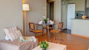 Un espace de vie compact comprenant un canapé, une table à manger avec des chaises, une lampe et un coin cuisine équipé d’appareils électroménagers.