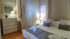 Une chambre d’hôtel avec un lit, une commode, une table de chevet, une lampe et une fenêtre avec des rideaux.