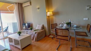 Un salon moderne avec un canapé, une table à manger en verre préparée pour deux personnes et un téléviseur.