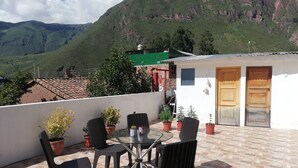 A terrace with wicker chairs and a glass table, surrounded by potted plants, overlooking a mountainous landscape. - vrinda wasi 108 (Lamay)