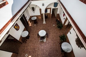 Un patio con cuatro mesas redondas y sillas, rodeado por muros blancos con escudos decorativos.