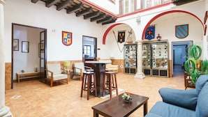 A spacious indoor area with a high ceiling, a dining table with chairs, a sofa, and a display cabinet with various items. - Hotel Carlos V by Viverestays (Jerez de la Frontera)