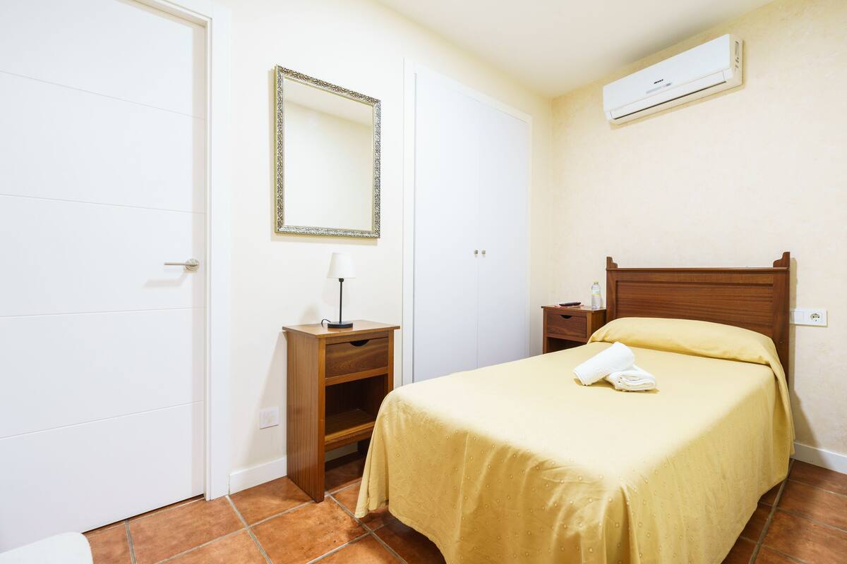 Un dormitorio con cama, mesita de noche, cómoda, espejo y equipo de aire acondicionado.