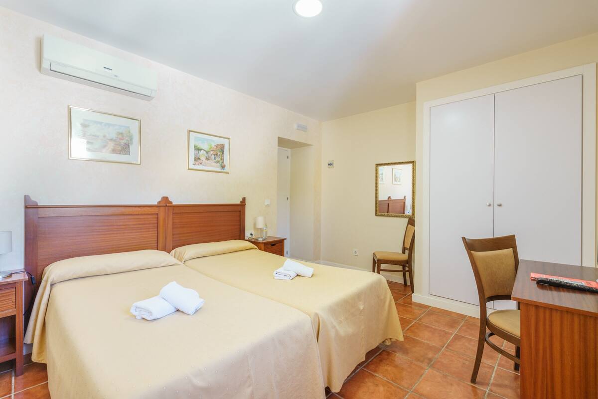 Habitación de hotel con dos camas, un escritorio, una silla, un armario y la puerta del baño.