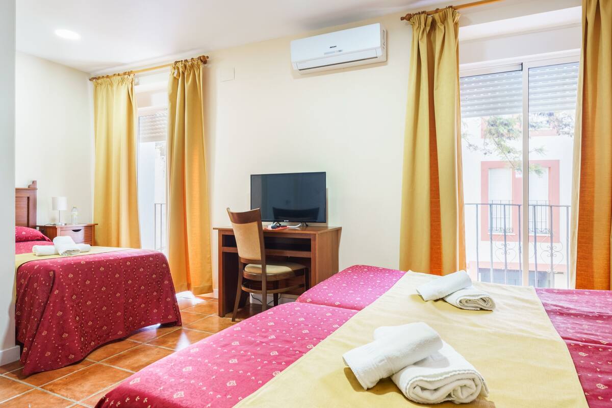 Habitación de hotel con dos camas, un escritorio con silla, un televisor y un equipo de aire acondicionado.