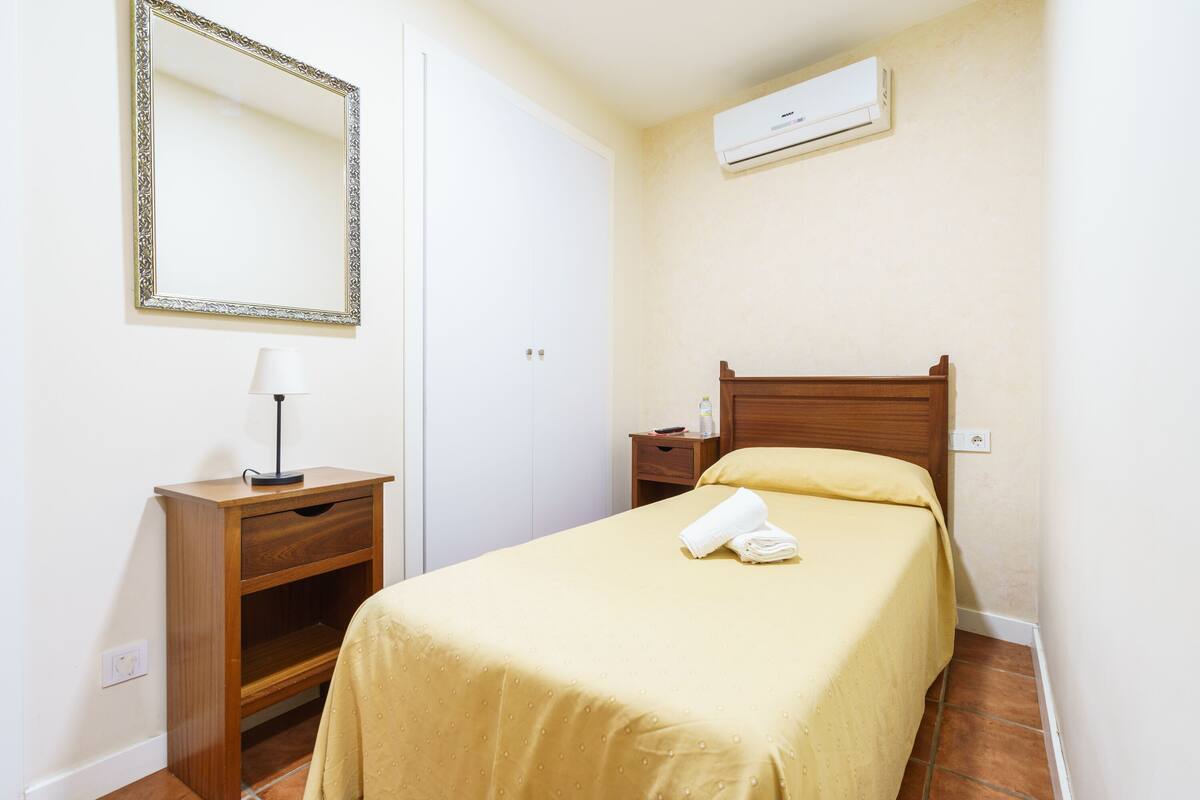 Una habitación de hotel con una cama, una mesita de noche, una lámpara, un espejo y un equipo de aire acondicionado.