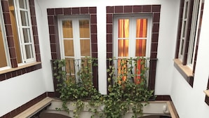 A courtyard with a central column, tiled walls, and a balcony with plants. - Hotel Carlos V by Viverestays (Jerez de la Frontera)