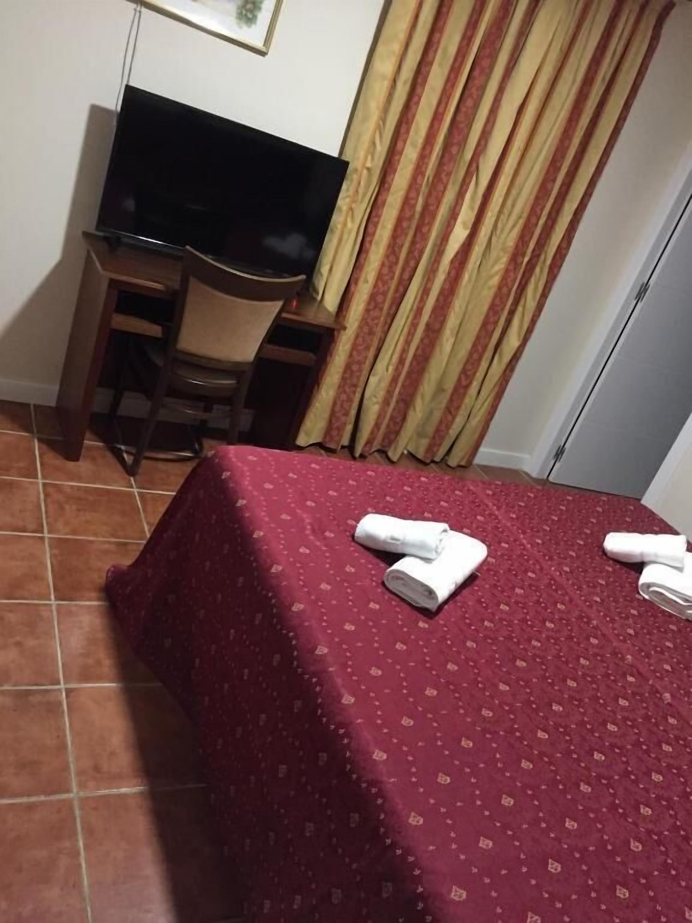 Ein Hotelzimmer mit Bett, Schreibtisch, Stuhl, Fernseher und Vorhang.