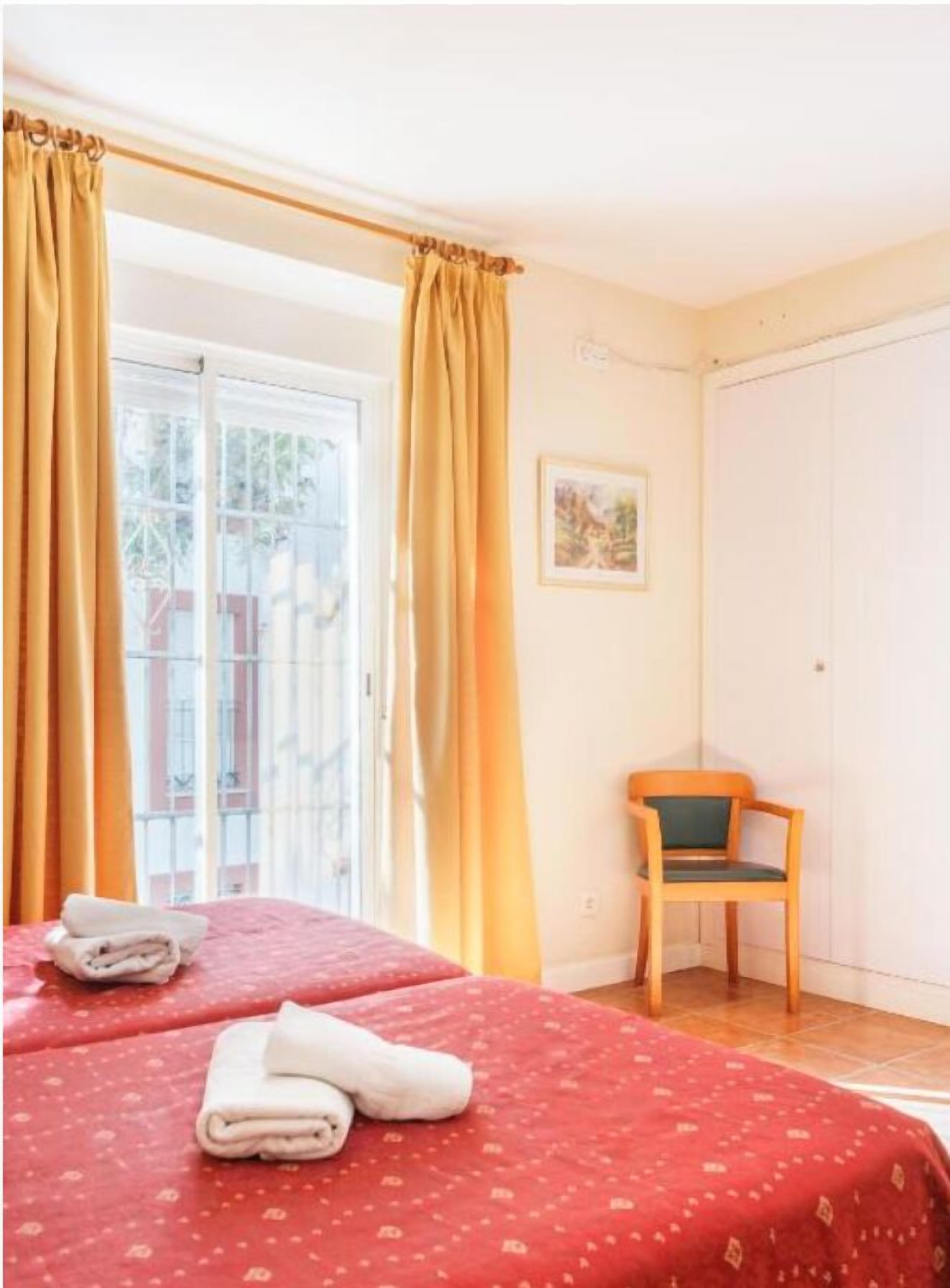 A hotel room with two beds, a chair, and a door.
