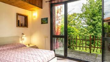 Camera da letto con un letto, un comodino, uno specchio a parete e una finestra vista verde.